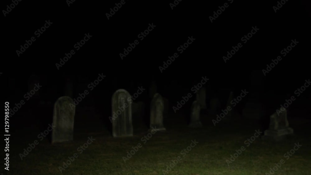 Dark pan across cemetery graveyard at night