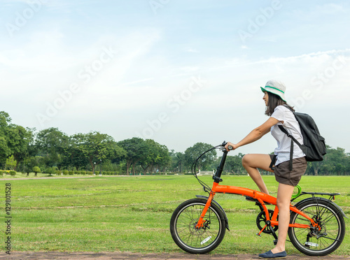 Young woman with backpack standing with bicycle in park, travel