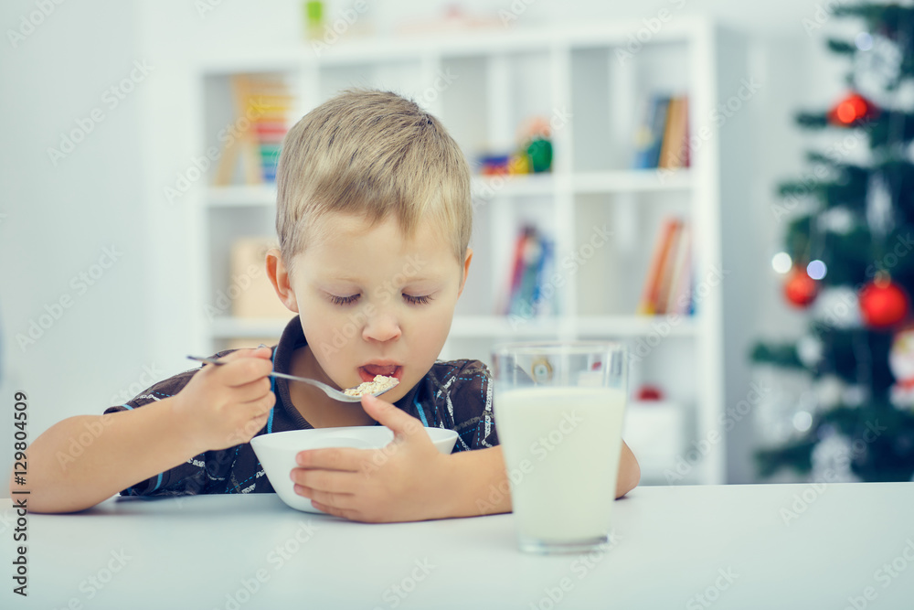 Waiting for Christmas. Little boy eating breakfast on the eve of the new year. Christmas tree in the background. Waiting for Christmas. Little boy eating breakfast on the eve of the new year. Christmas tree in the background.