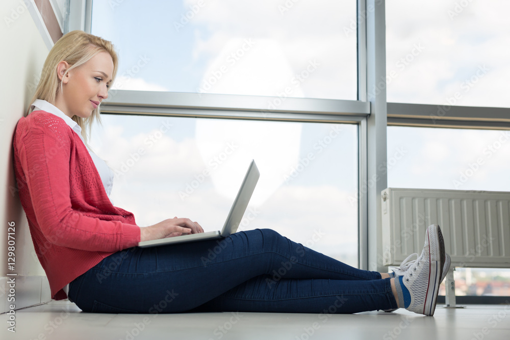 Happy young woman sitting on the floor with crossed legs and usi Happy young woman sitting on the floor with crossed legs and usi
