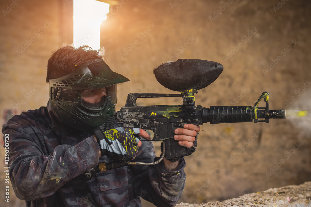 Paintball player in protective uniform shooting target with gun Stock