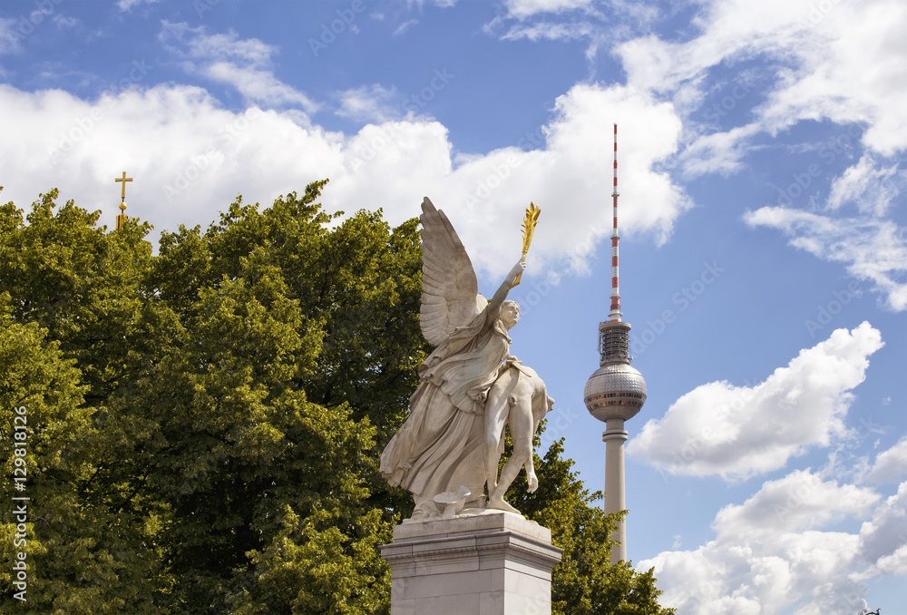 Φωτογραφία Winged woman statue on Schlossbruecke bridge with trees, cloudy sky and TV tower in the background