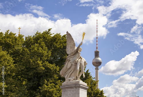 Winged woman statue on Schlossbruecke bridge with trees, cloudy sky and TV tower in the background. Designed by K. F. Schinkel in 1821 with sculptures of gods. photo