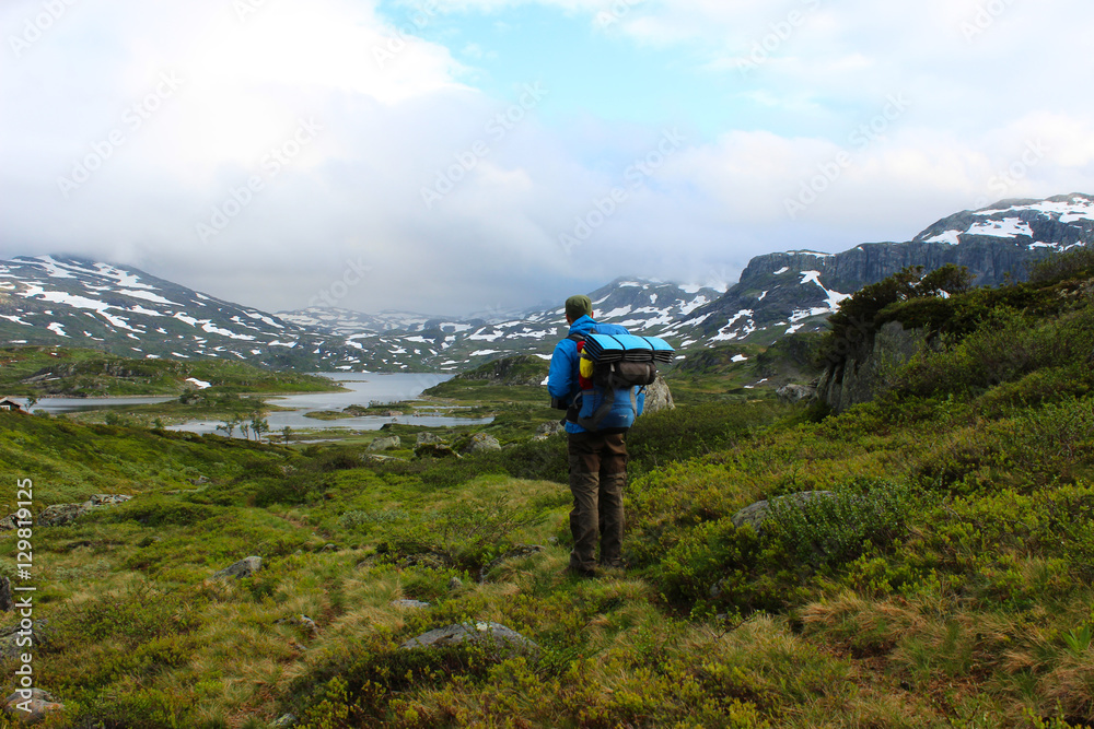Wanderer im grünen Hochland Norwegens. Wanderer zentriert im Bild blickt in die Weite der Landschaft. Schneebedeckte Berge am Horizont
