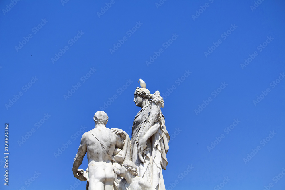 Pigeon on top of statue in front of Altar of the Fatherland with clear, blue sky background. Grand marble, classical temple honoring Italy's first king & First World War soldiers.