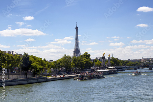 Tour boats are on Seine River in Paris. Trees, Pont Alexandre III bridge and Eiffel tower are in the view.