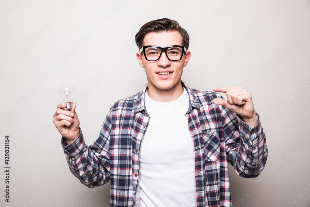 Cheerful young man in glasses holding light bulb and showing small size over black backgorund Cheerful young man in glasses holding light bulb and showing small size over black backgorund