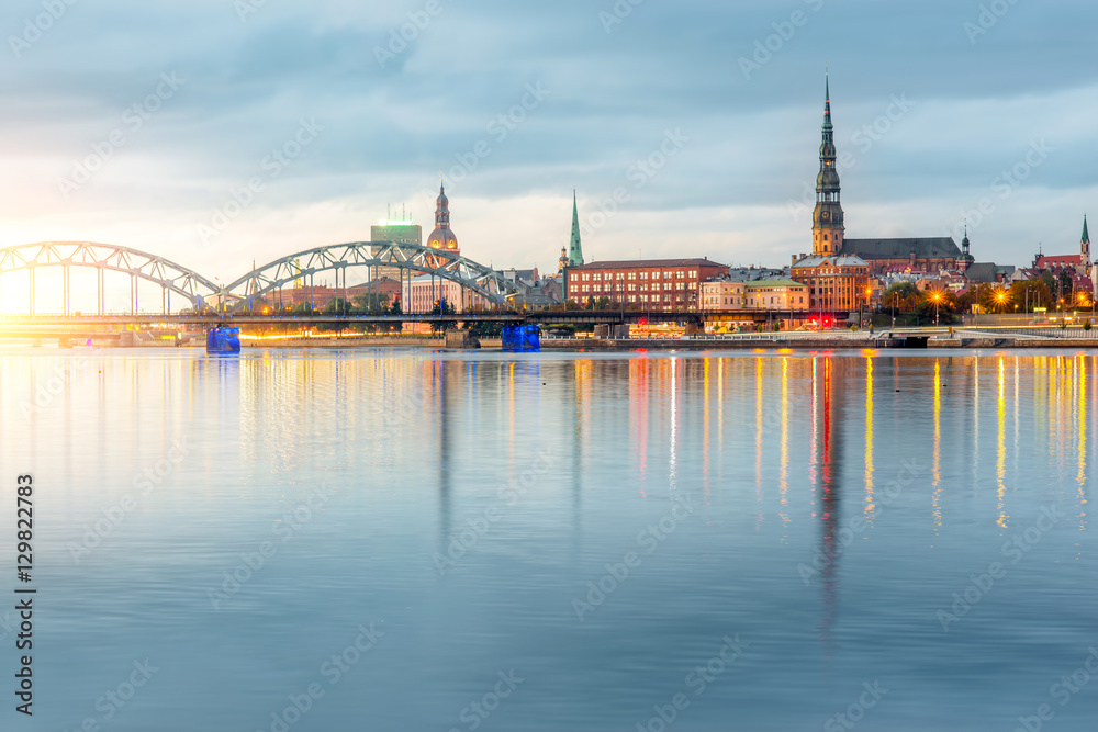 Night view on the illuminated riverside with reflection on the river in Riga, Latvia - obrazy, fototapety, plakaty 