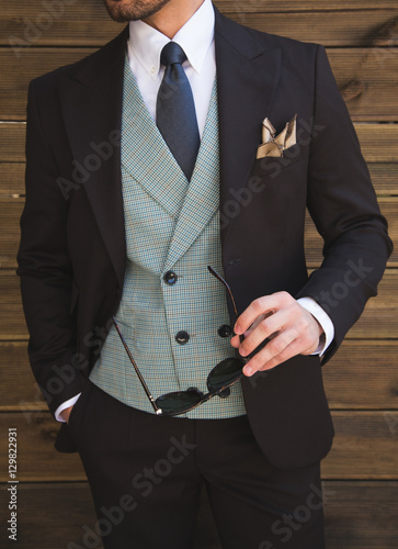 Male model in a three part suit posing in front of a wooden wall