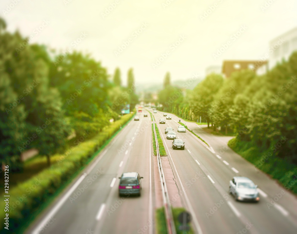 Right hand driving motorway with speedy cars surrounded by green backgrounds - Tilt shift lens used to accent motorway and to emphasize the speed vision