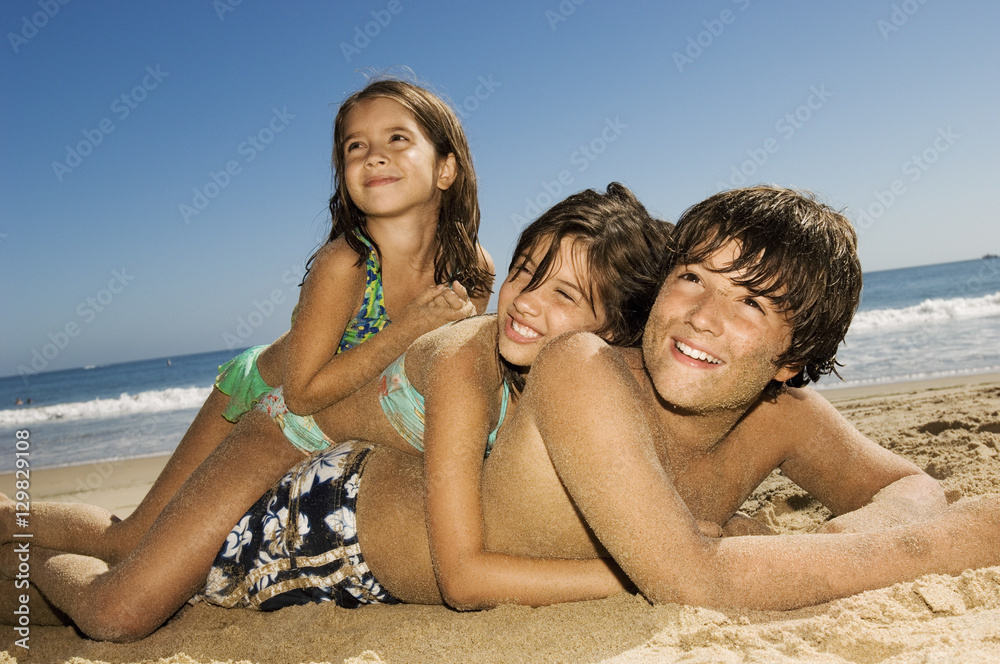 Cheerful children lying on top of each other while looking away at beach Cheerful children lying on top of each other while looking away at beach
