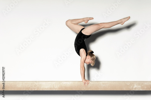 Photography Side view of a young female doing a handstand on balance beam