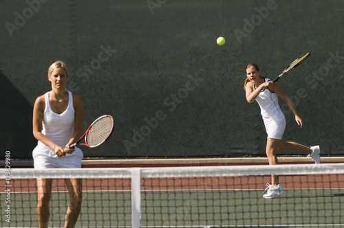Female tennis player standing with her partner hitting shot in background © moodboard