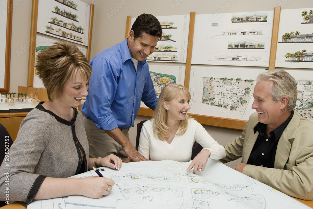 Obraz premium Happy couple and architects discussing plan for new house in office