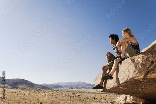 Full length of thoughtful rock climbers sitting on rock against clear blue sky