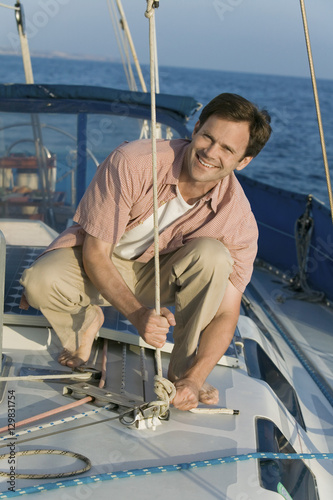 Portrait of happy mature man tying rope on the yacht during vacation