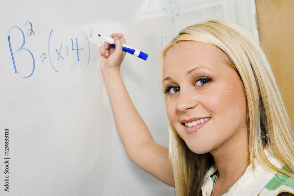 Closeup portrait of beautiful student solving algebra equation on whiteboard in classroom Closeup portrait of beautiful student solving algebra equation on whiteboard in classroom