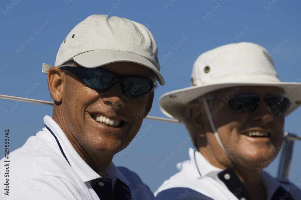 Closeup portrait of two smiling men in sunhats on yacht against clear blue sky Closeup portrait of two smiling men in sunhats on yacht against clear blue sky