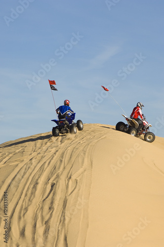 Two young men riding quad bikes on sand dune in desert