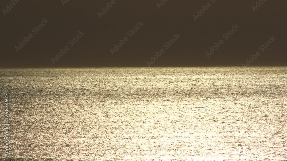 Golden Pacific Ocean, calm water with dark horizon.