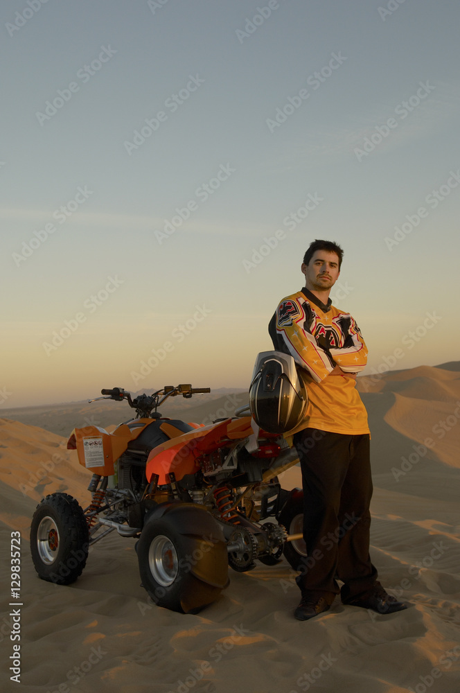 Full length of man standing with hands folded by quad bike in desert