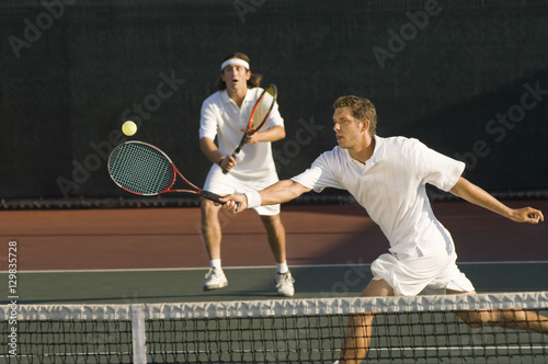 Young male tennis player hitting ball with doubles partner standing in background © moodboard
