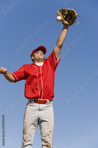 Baseball player trying to catch ball against clear sky