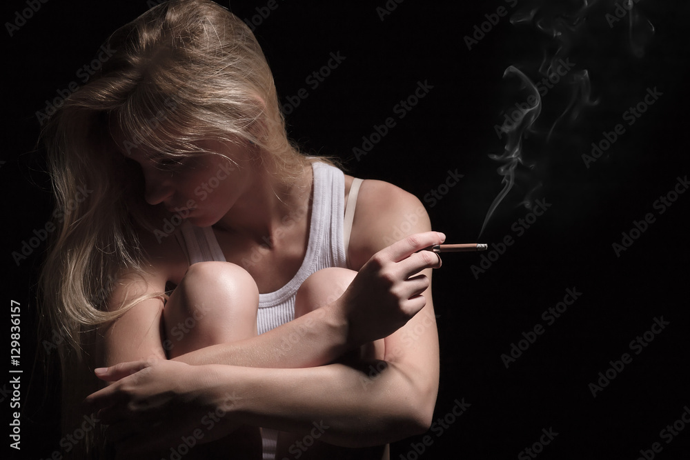 Obraz premium young woman sitting in dark smoking cigarette