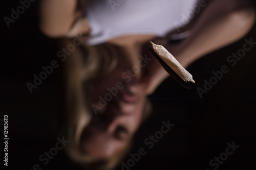 joint with marijuana on black mirror background with female blurred reflection