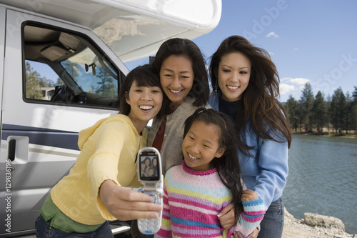 Three-generations of women photographing selves outside RV at lake