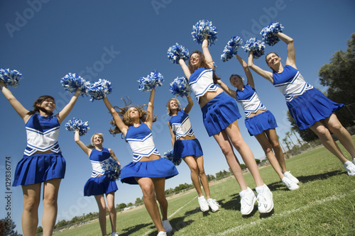 Group of excited young cheerleaders cheering on field photo