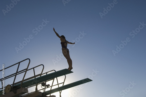 Low angle view of a female diver with arms out about to dive against the blue sky