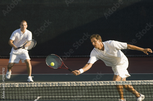 Mixed doubles player hitting tennis ball with partner in the background © moodboard