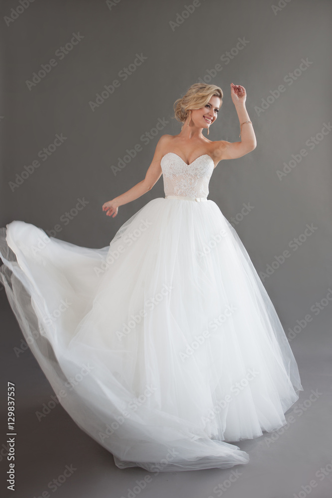 Naklejka premium Dancing young bride in luxurious wedding dress. Pretty girl in white. Emotions of happiness, laughter and smile, gray background