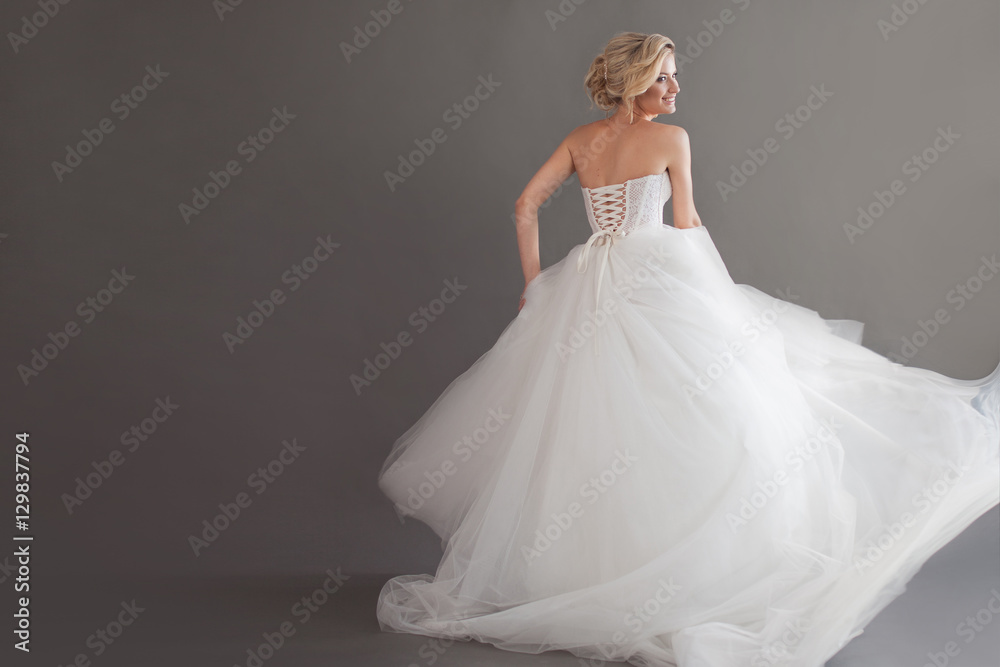 Dancing young bride in luxurious wedding dress. Pretty girl in white. Emotions of happiness, laughter and smile, gray background