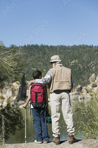 Rear view of grandfather standing with grandson holding a fishing net nearby a lake