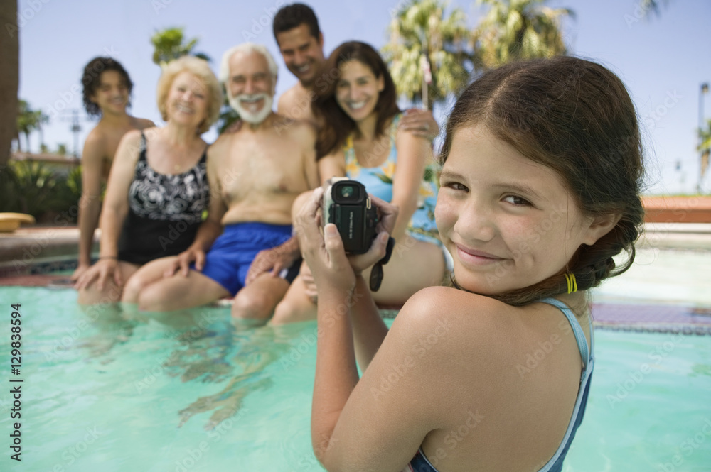 Portrait of smiling girl with video camera recording family in swimming pool