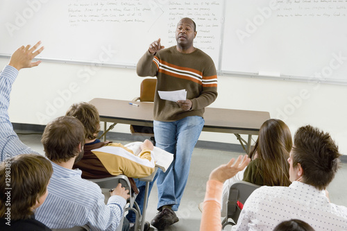 Professor pointing at college student with hands raised in classroom photo