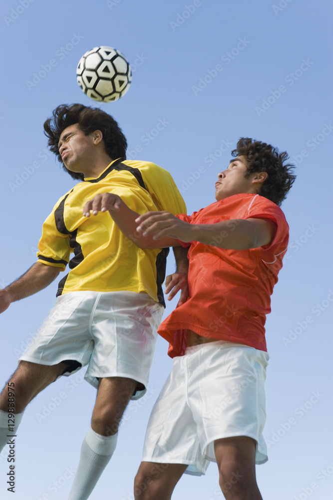 Fototapeta premium Low angle view of young soccer players heading ball against clear blue sky