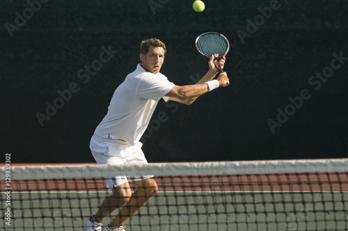 Male tennis player hitting backhand by net on the tennis court © moodboard