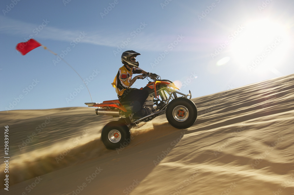 Side view of a man riding quad bike in desert on a sunny day Stock