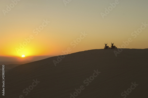 Silhouette of quad bikers in desert at sunset