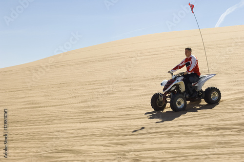 Side view of a man riding quad bike in desert on a sunny day