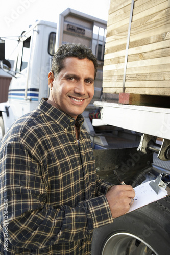 Portrait of a smiling male supervisor with clipboard by truck loaded with wood