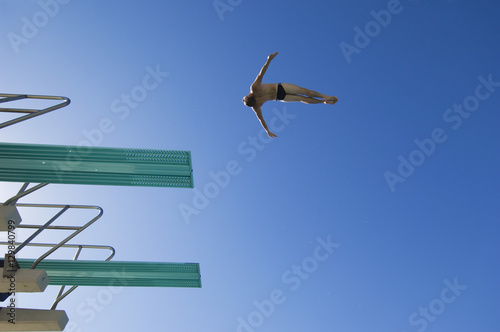 Low angle view of a male swimmer preparing to dive from diving board against clear blue sky