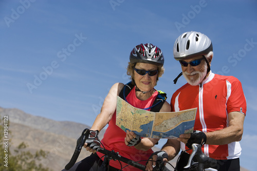 Happy senior bicyclists reading map together