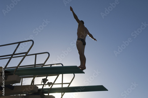 Low angle view of a male diver with arms out about to dive against the blue sky