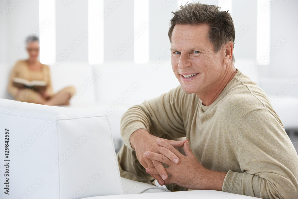 Portrait of smiling man with hands clasped with woman in background at home Portrait of smiling man with hands clasped with woman in background at home