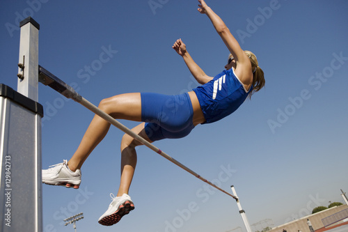 Female athlete performing high jump against sky