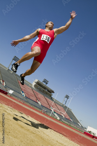 Full length of a male athlete doing a long jump into a sandpit
